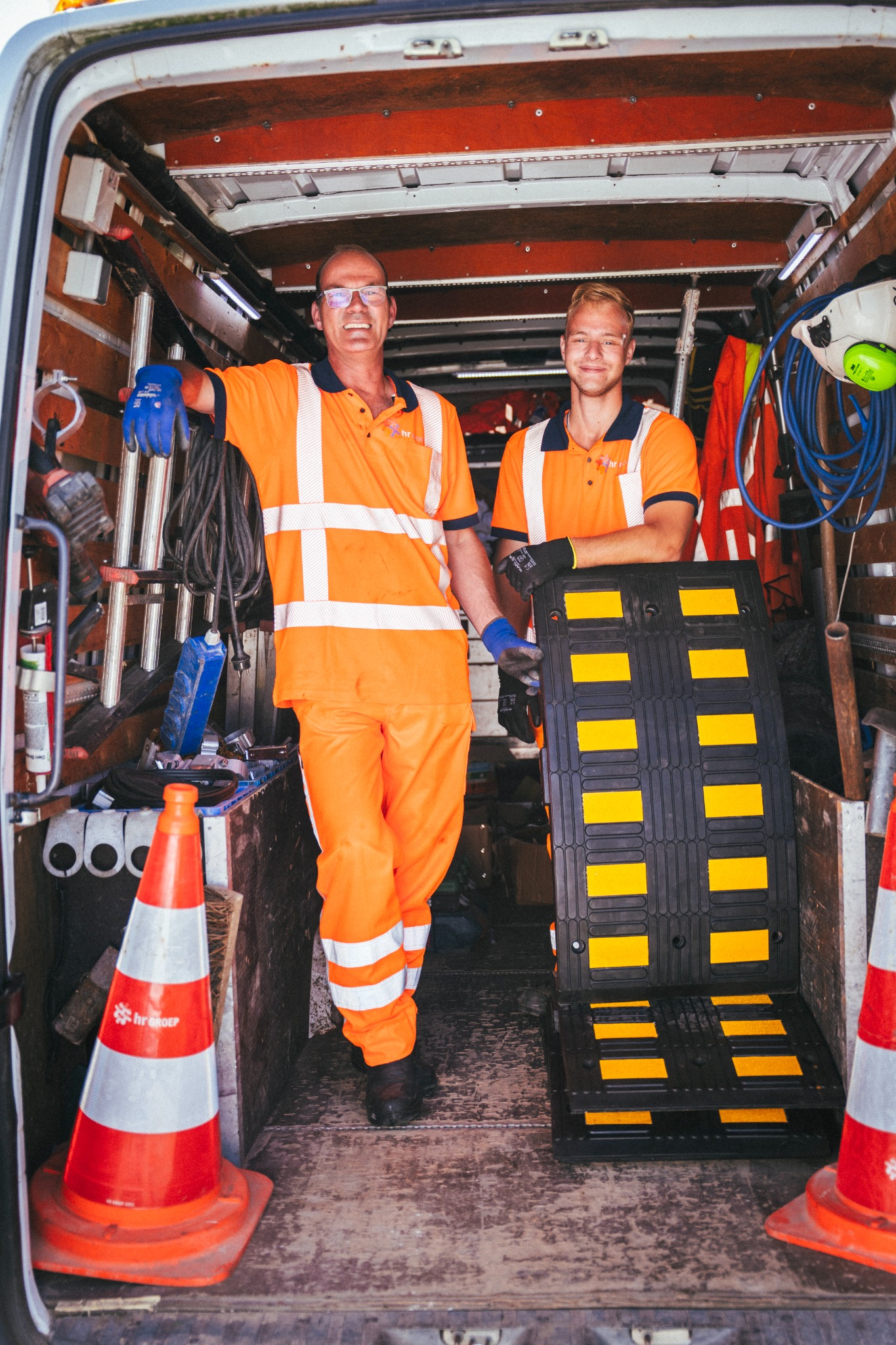 Twee medewerkers van HR Groep bij hun werkbus met een verkeersdrempel