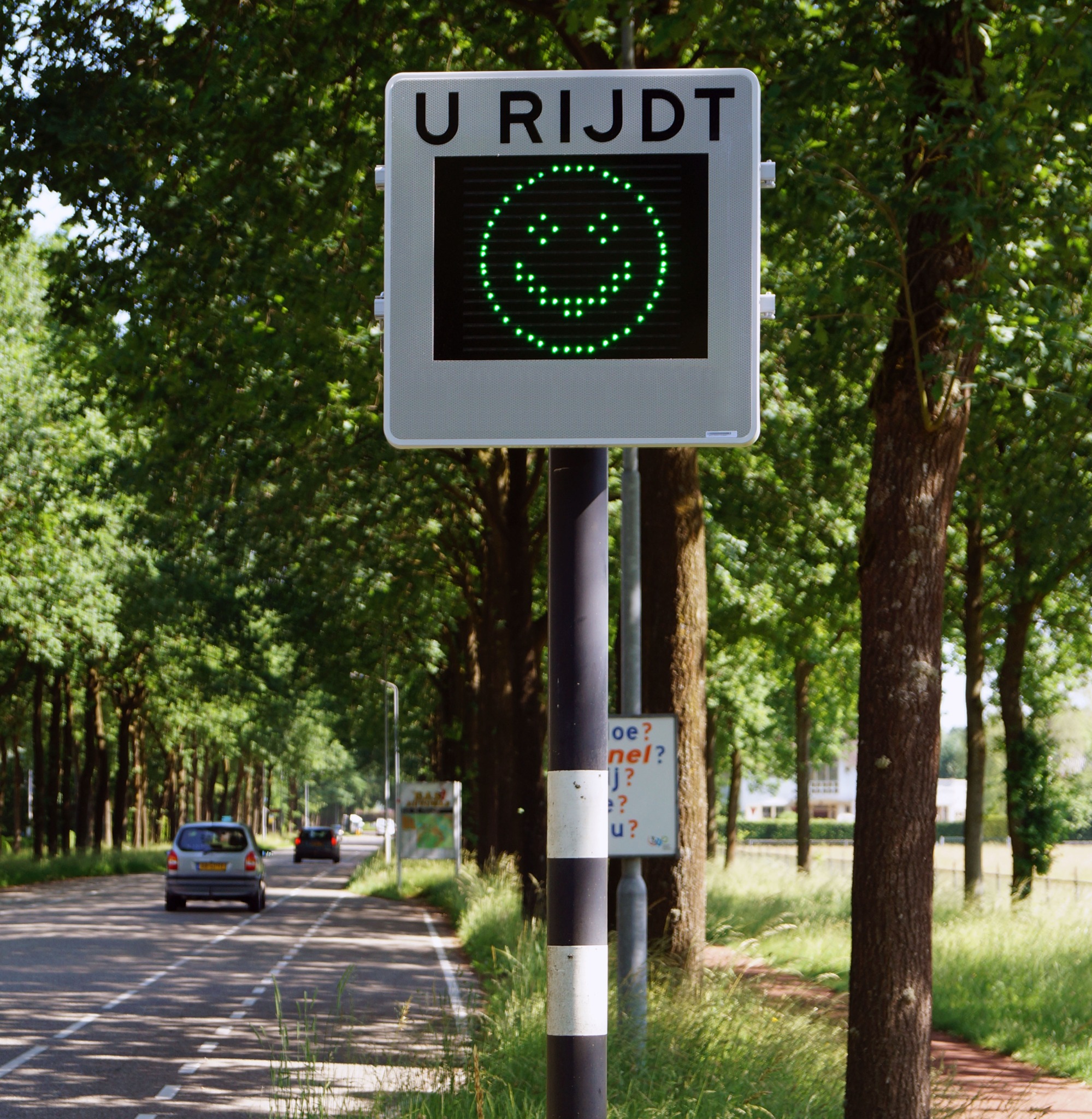 Snelheidsdisplay met een groene smiley langs een weg
